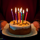 Hands holding out a birthday cake with candles lit